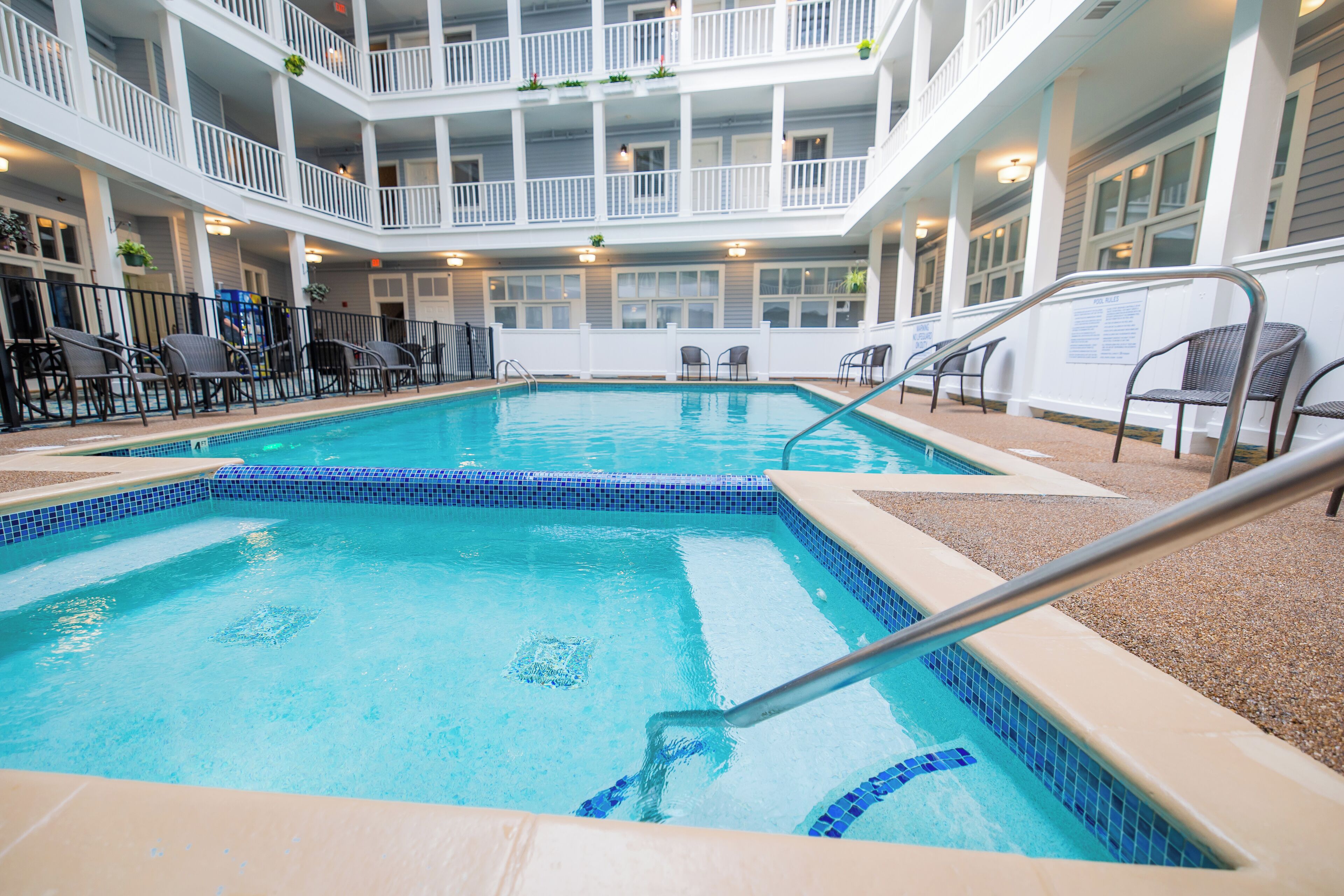 An indoor swimming pool with a tiled edge, surrounded by lounge chairs and a balcony with railings.