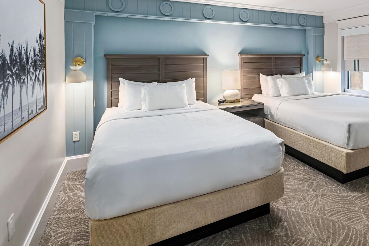 A hotel room with two beds, a large mirror, and a wall-mounted artwork.