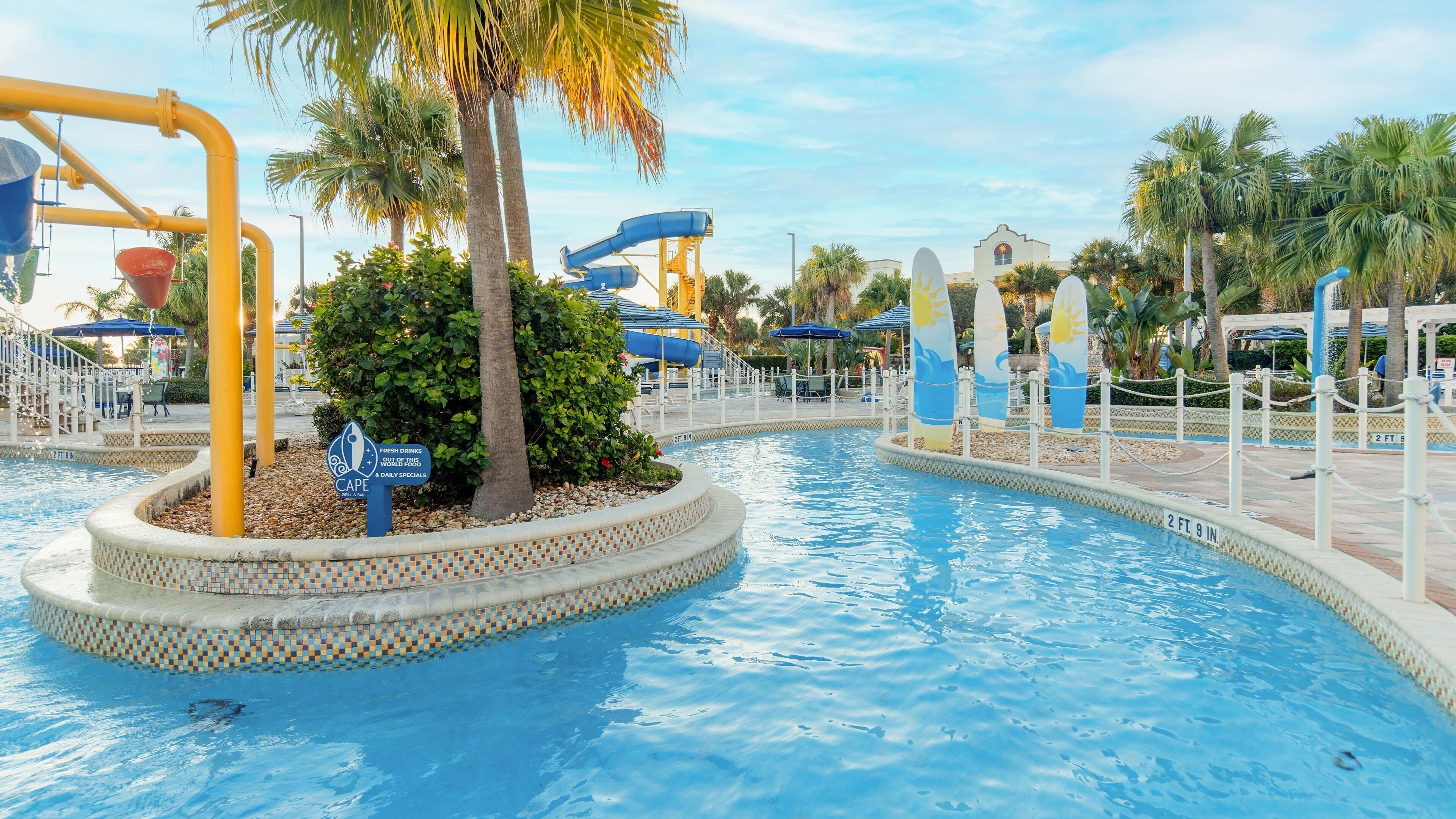 A pool area with a water slide, palm trees, and a sign for a restaurant.