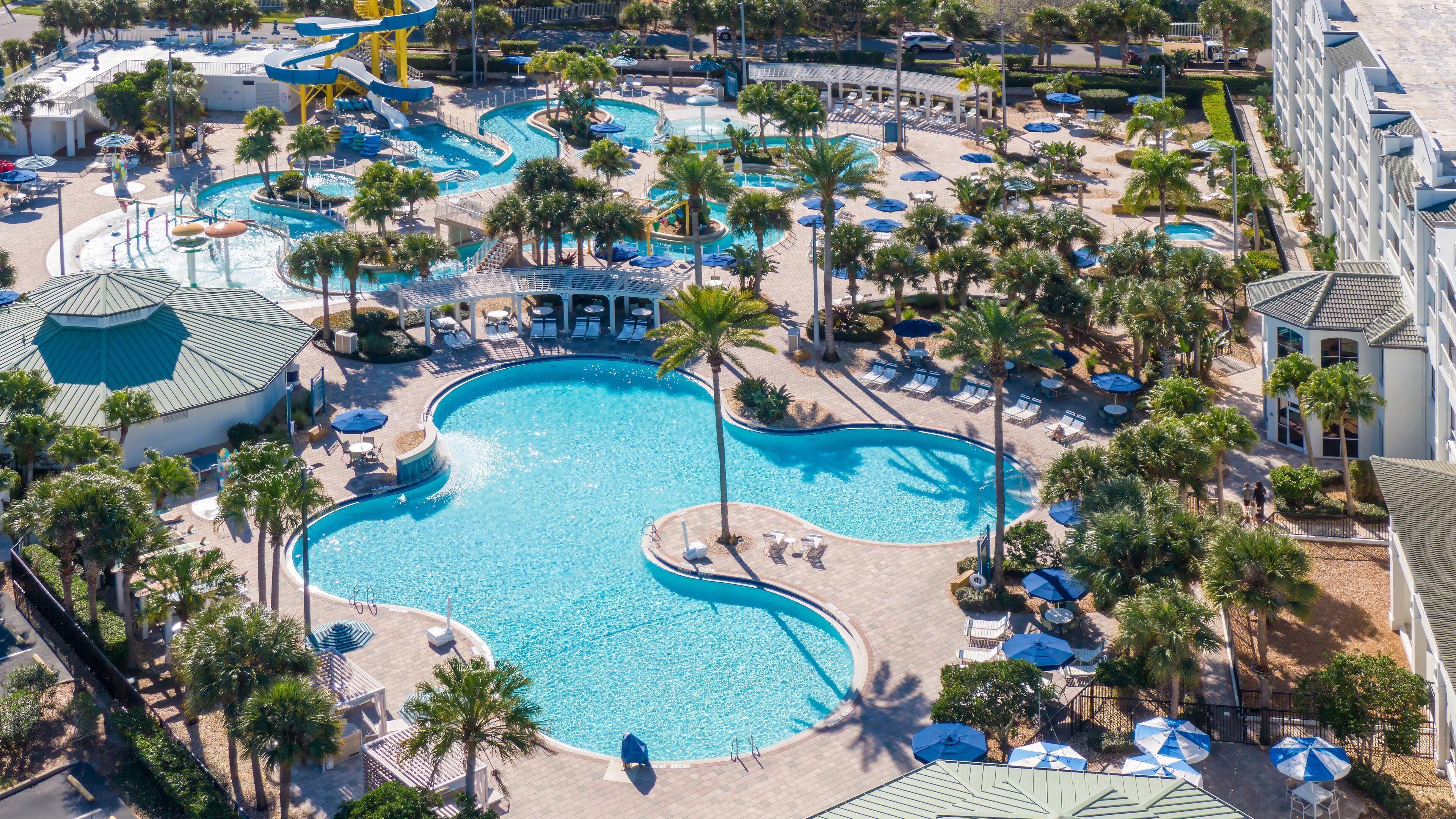 Un complexe hôtelier doté de plusieurs piscines, de palmiers et de chaises longues.