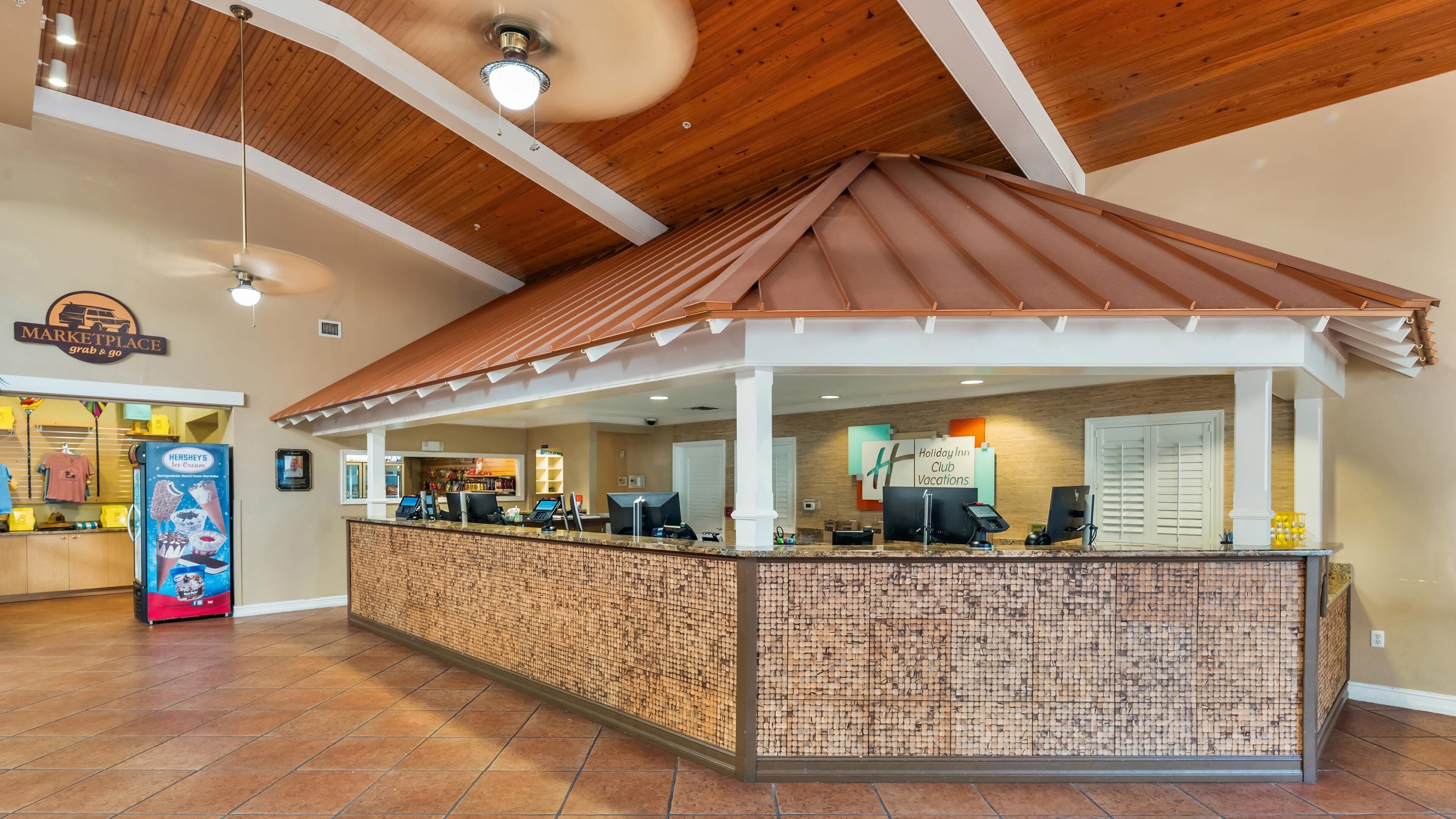 Un'area reception con soffitto in legno, un banco con computer e un cartello per Holiday Inn Club Vacations.