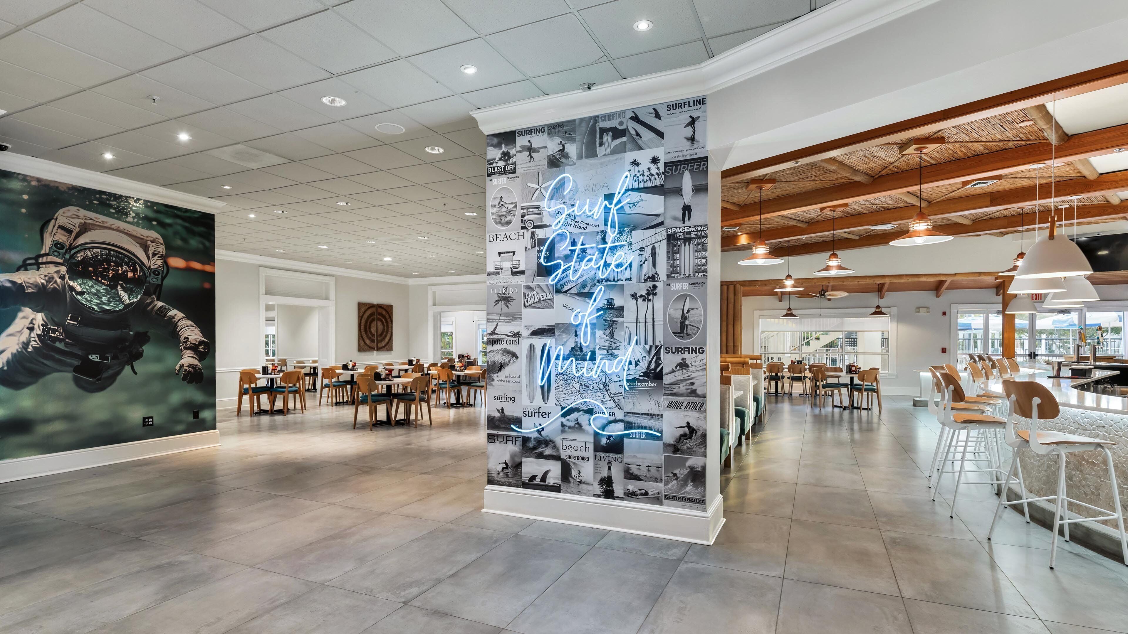 Un'ampia sala ristorante con soffitti alti e illuminazione moderna, caratterizzata da un grande murale e un'imponente vetrina verticale.