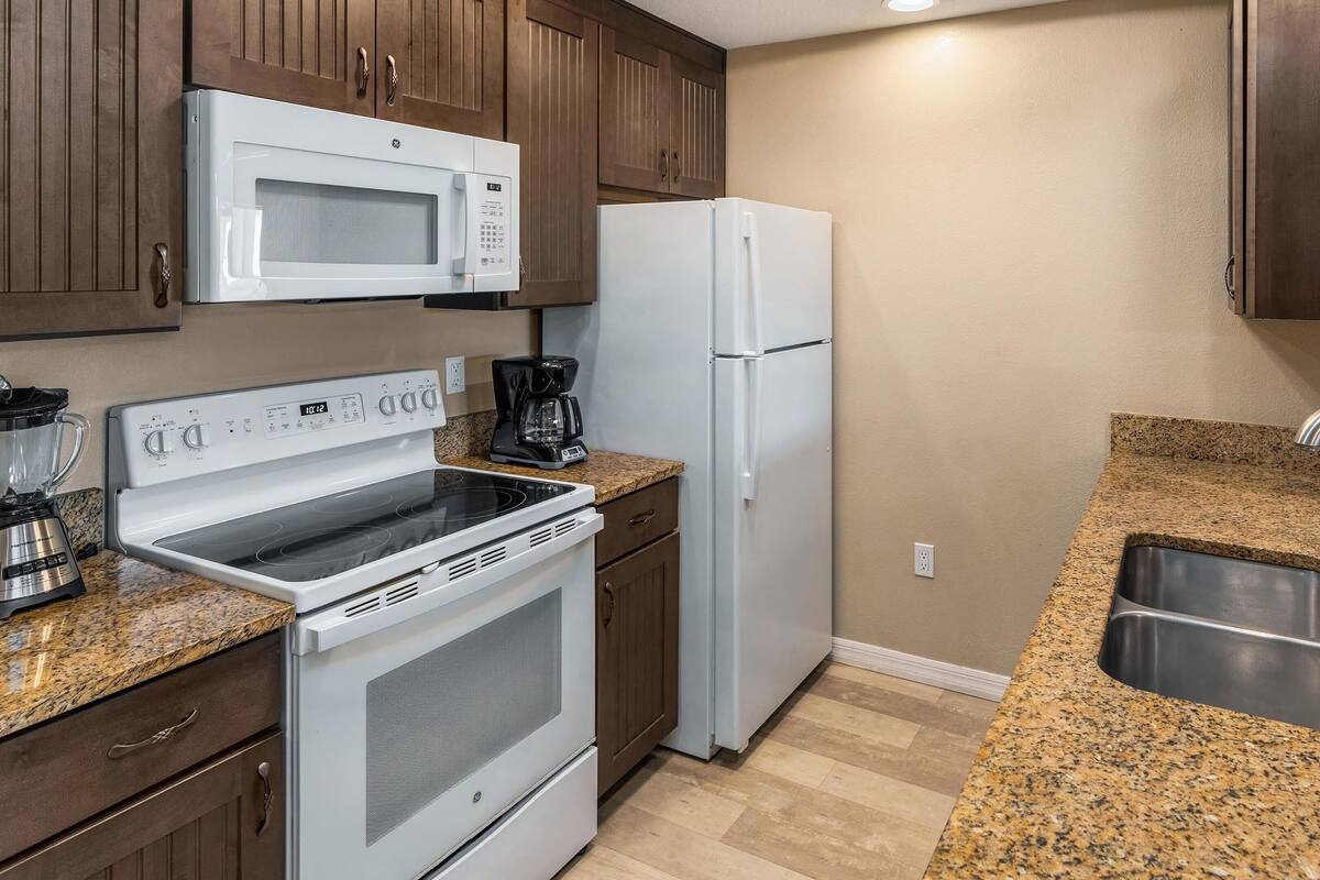 A kitchen with a microwave, refrigerator, stove, and granite countertops.