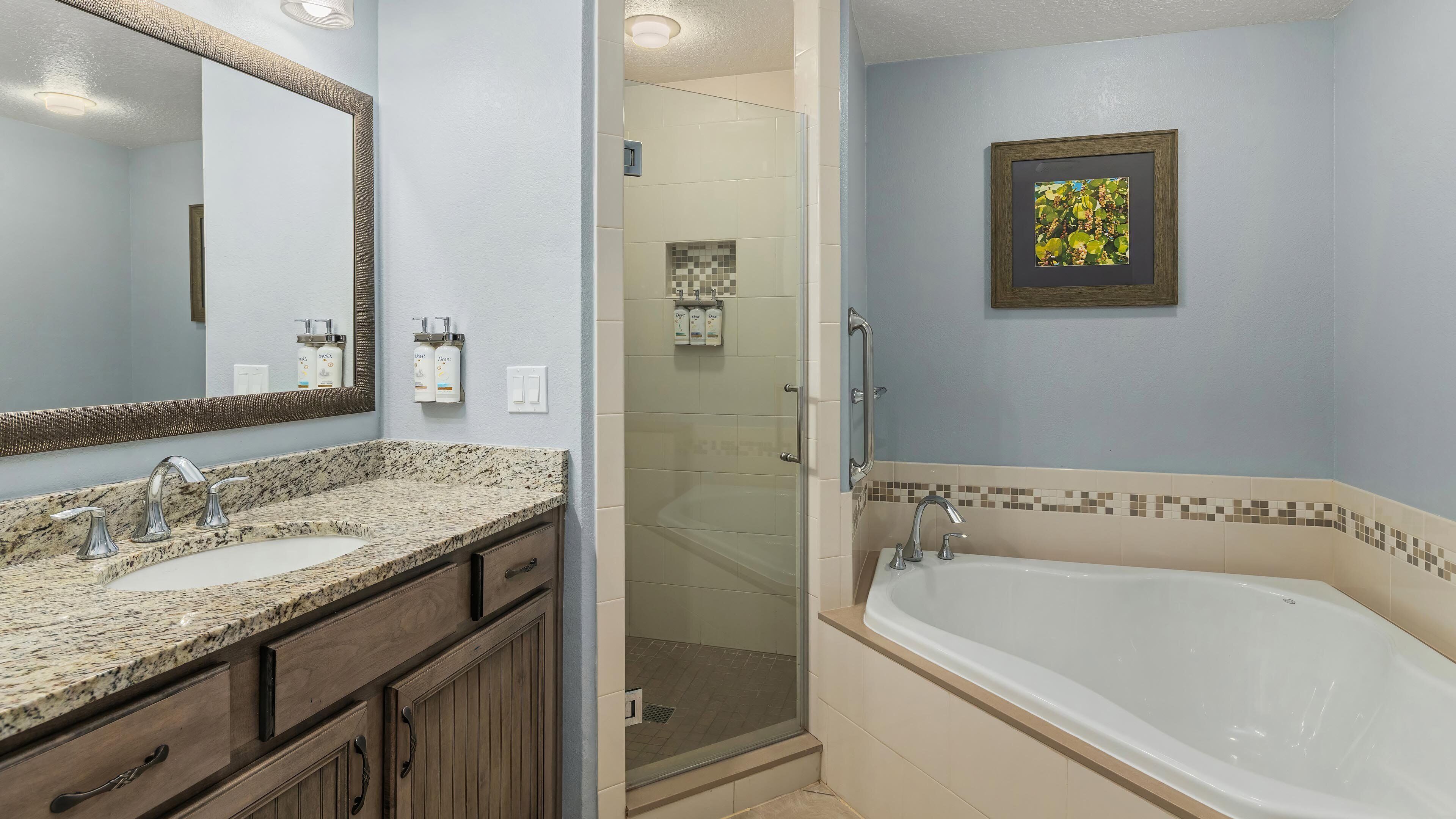 A bathroom with a double sink, a large bathtub, a shower enclosure, and a framed picture on the wall.