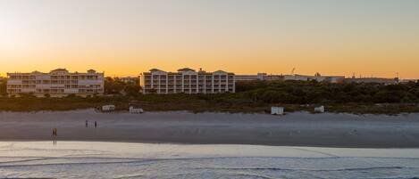 A beachfront hotel with multiple floors, a sandy beach in the foreground, and a clear sky.