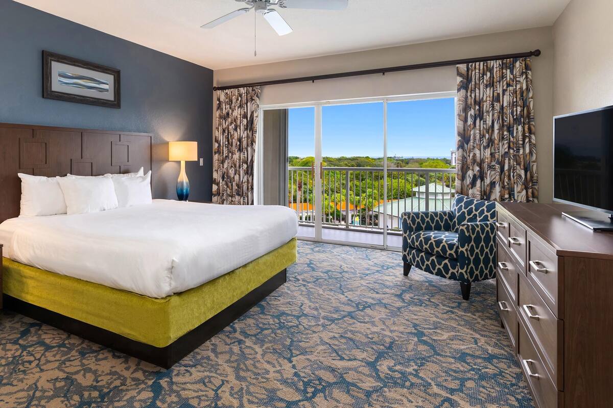 A hotel room with a bed, a television, a desk, and a balcony with a view.