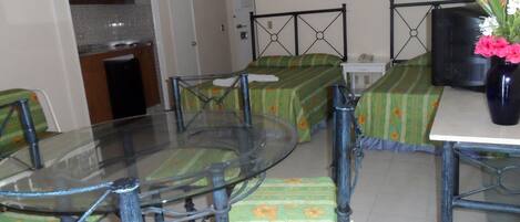A dining area with a glass table and chairs, a television, and a vase with flowers.
