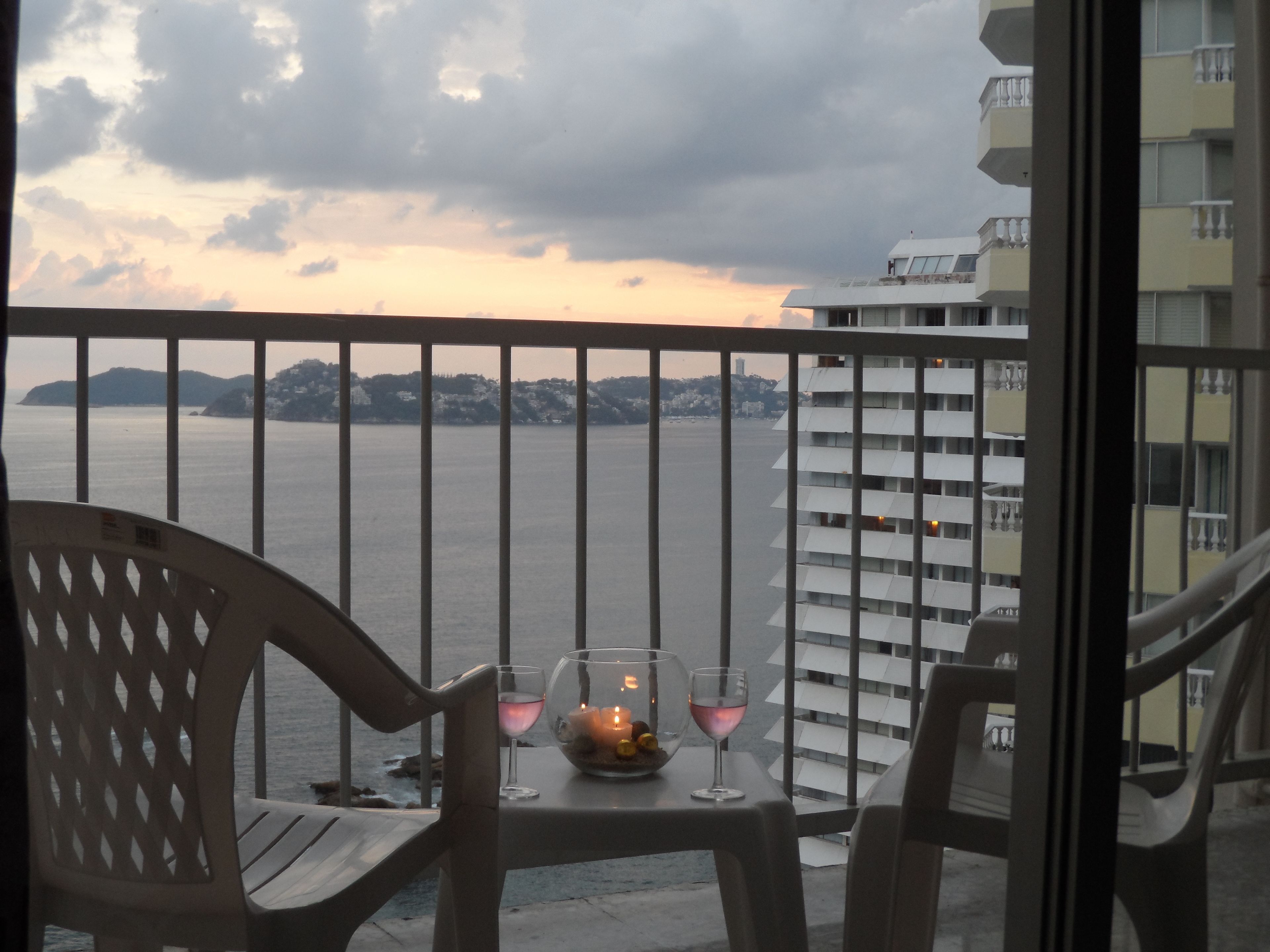 A balcony with a table set for two, overlooking a body of water and a distant shoreline.
