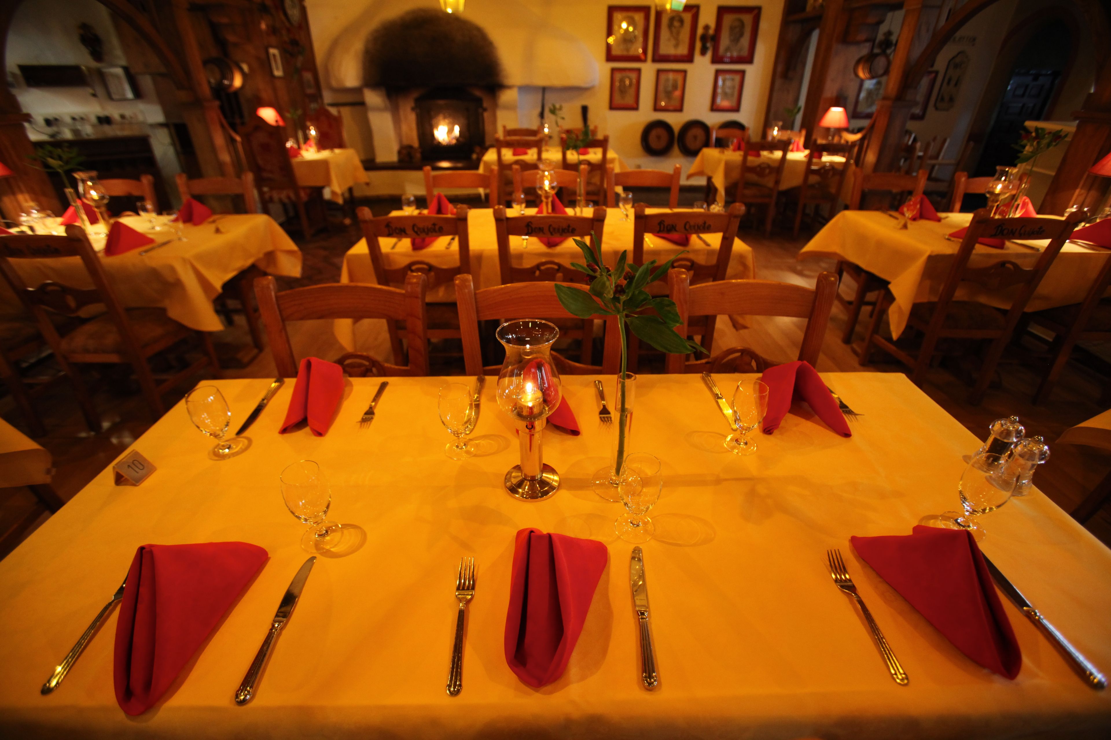 Un restaurant où les tables sont dressées pour le service, avec des serviettes rouges, des couverts en argent et des verres à vin.
