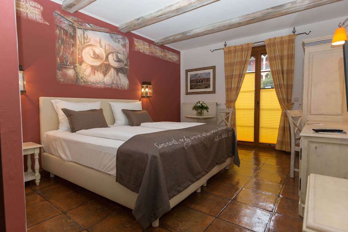 A bedroom with a bed, bedside tables, a desk, a chair, a lamp, and a window with curtains.