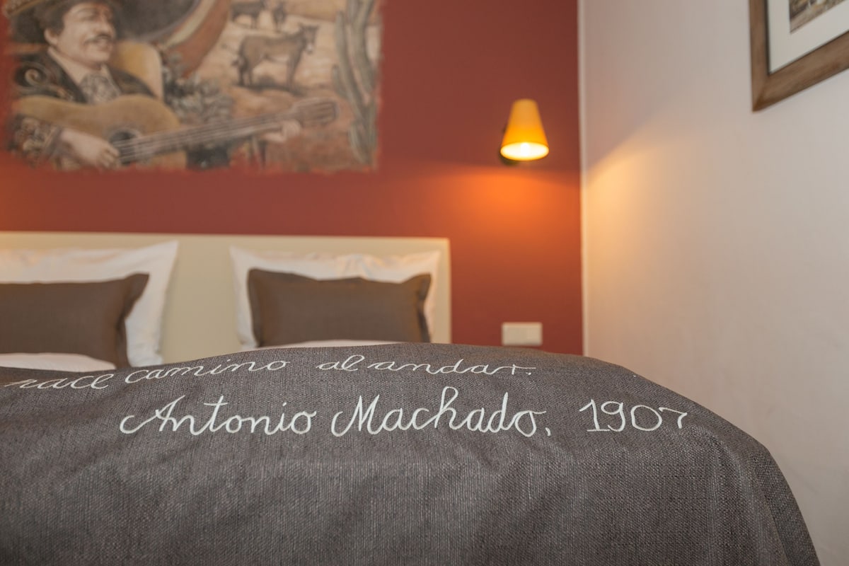 A hotel room with a bed, pillows, a painting on the wall, and a lamp.
