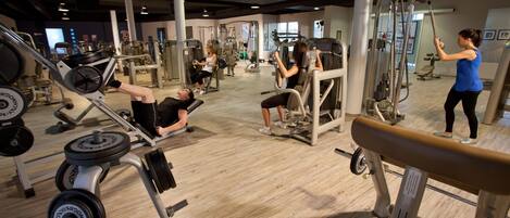 A gym with various exercise machines, weights, and a wooden floor.