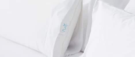 A white bed with pillows, one of which has a label that reads "Pure."