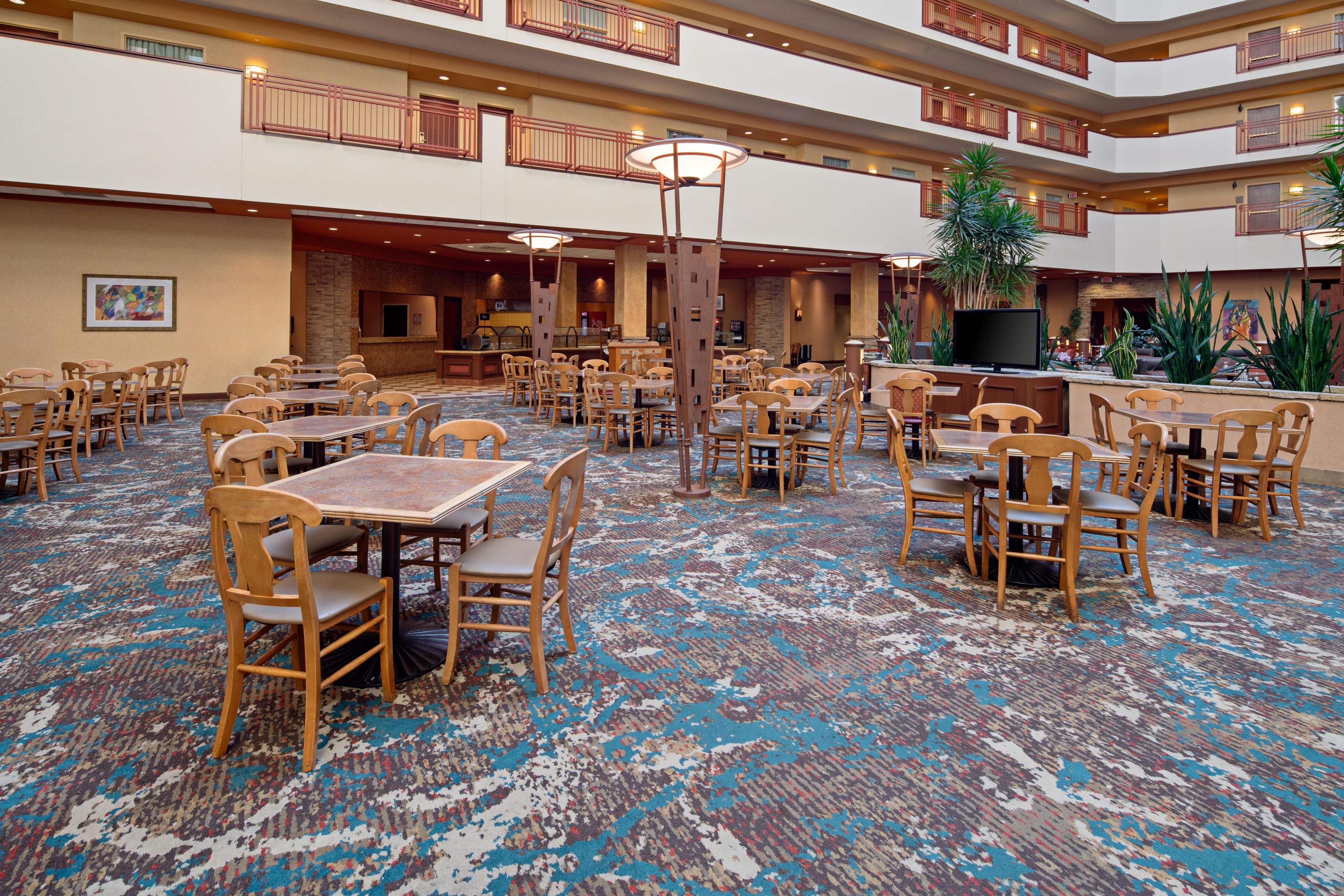 Un hall d’hôtel doté de plusieurs espaces de restauration, d’une grande table centrale et d’un écran de télévision.
