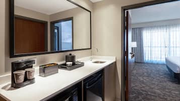 Habitación de hotel con una encimera blanca, un lavabo, un espejo, una cafetera y una cama con vistas.