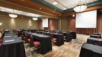 Una sala de conferencias con varias mesas, sillas y una pantalla grande.