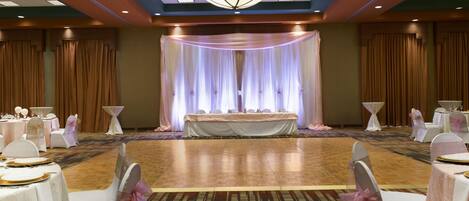 A banquet hall with a central stage, round tables with white tablecloths, and chairs with pink sashes.