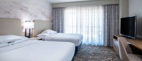 A hotel room with two beds, a TV, a desk, and a chair.