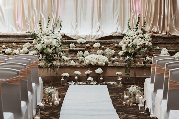 Une allée de cérémonie de mariage agrémentée de chaises blanches, de compositions florales et de bougies.