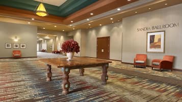 Un hall espacioso con una gran mesa de madera, un jarrón con flores rojas y un cartel para el salón Sandia.