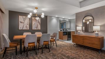 Habitación de hotel con comedor, kitchenette, espejo grande y alfombra estampada.