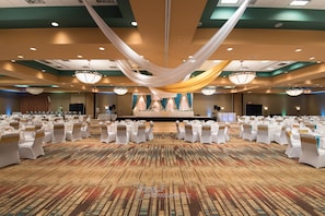 Une vaste salle de banquet, avec de longues rangées de tables et de chaises blanches, recouvertes de tissu blanc et doré.