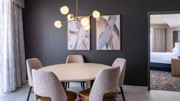 Un hotel moderno con una mesa redonda de comedor, seis sillas tapizadas, una araña, arte abstracto en la pared y vistas al dormitorio.