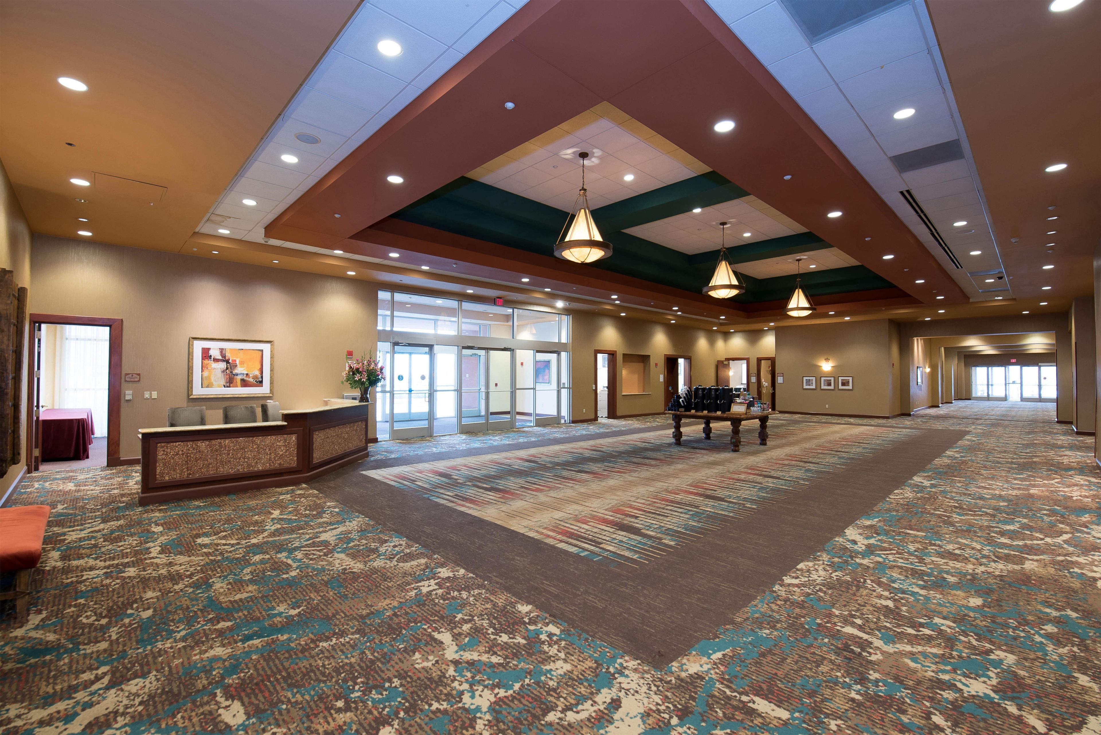 A spacious hotel lobby with a reception desk, a large carpeted area, and a high ceiling with recessed lighting.