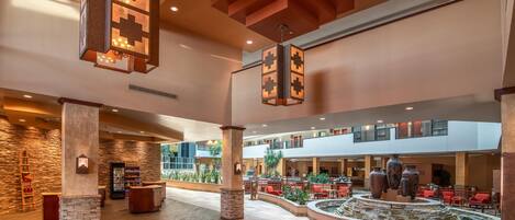 Um amplo saguão com uma fonte central, várias áreas de estar e um balcão de recepção.