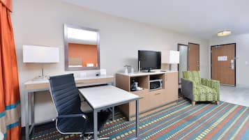 A hotel room with a bed, desk, chair, television, and a patterned carpet.