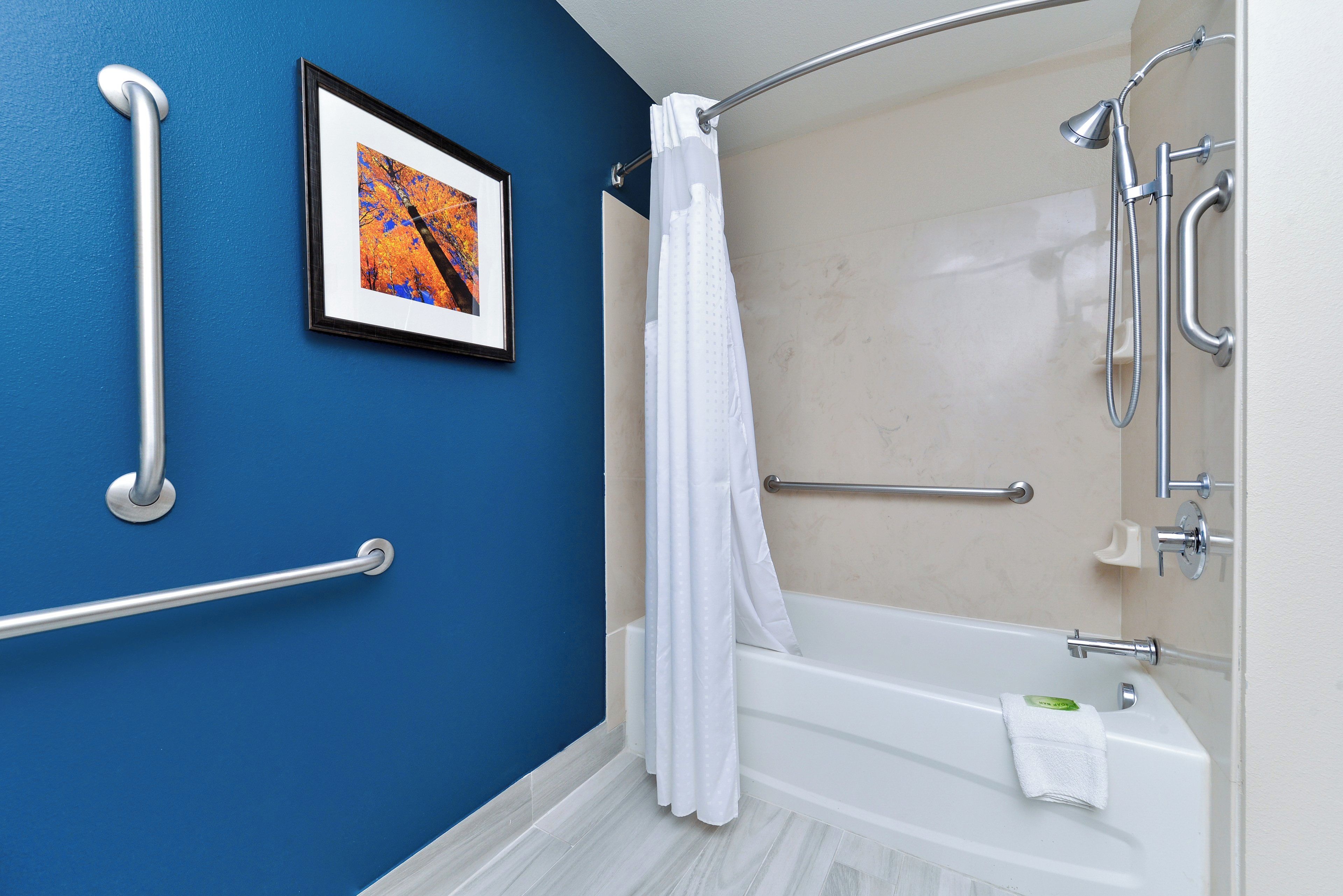Un baño con bañera, ducha y barras de apoyo.