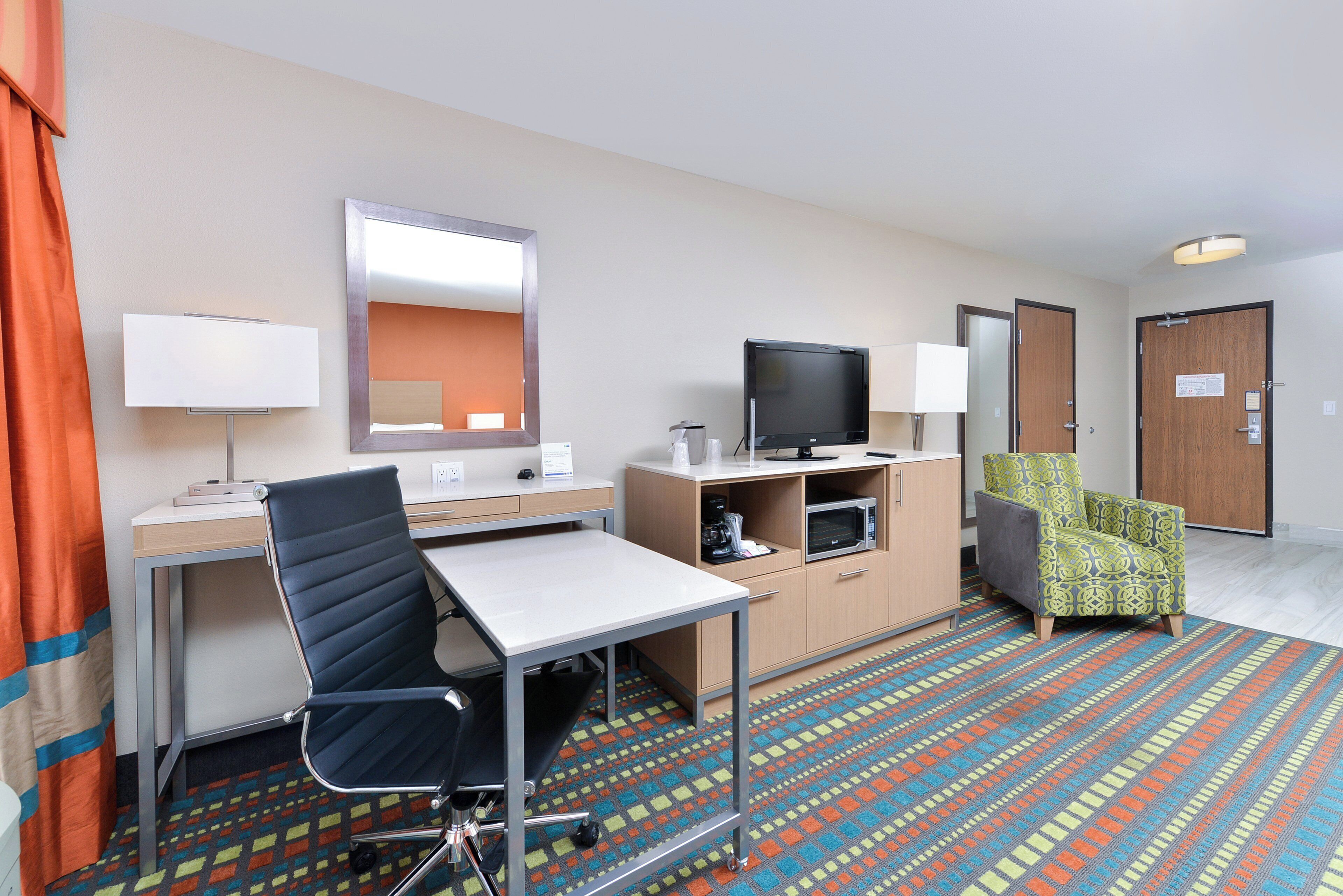 A hotel room with a desk, chair, television, and a patterned carpet.