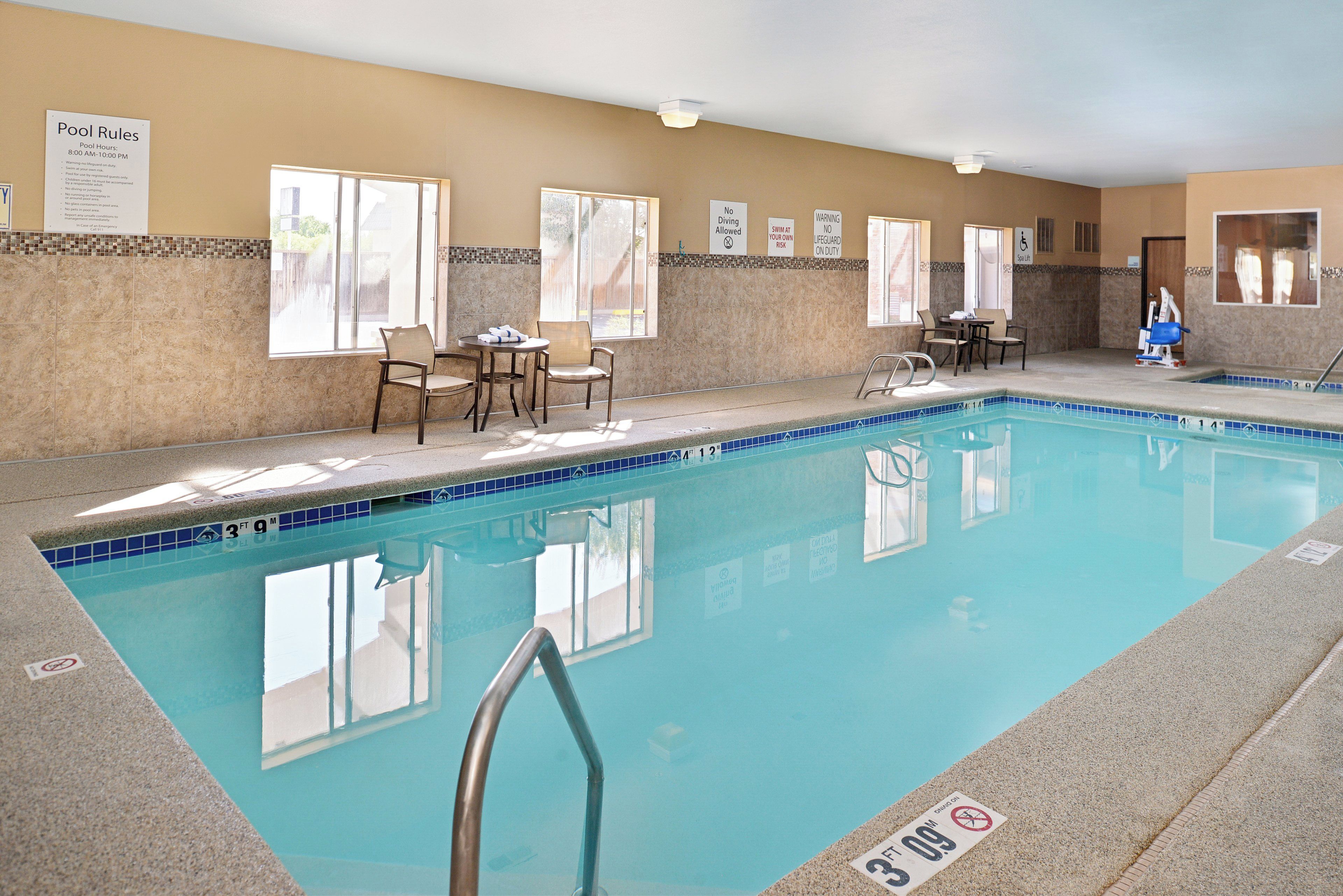 An indoor swimming pool with clear pool rules posted on the wall, a lifeguard chair, and a spa lift.