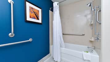 A bathroom with a bathtub, shower, and handrails.
