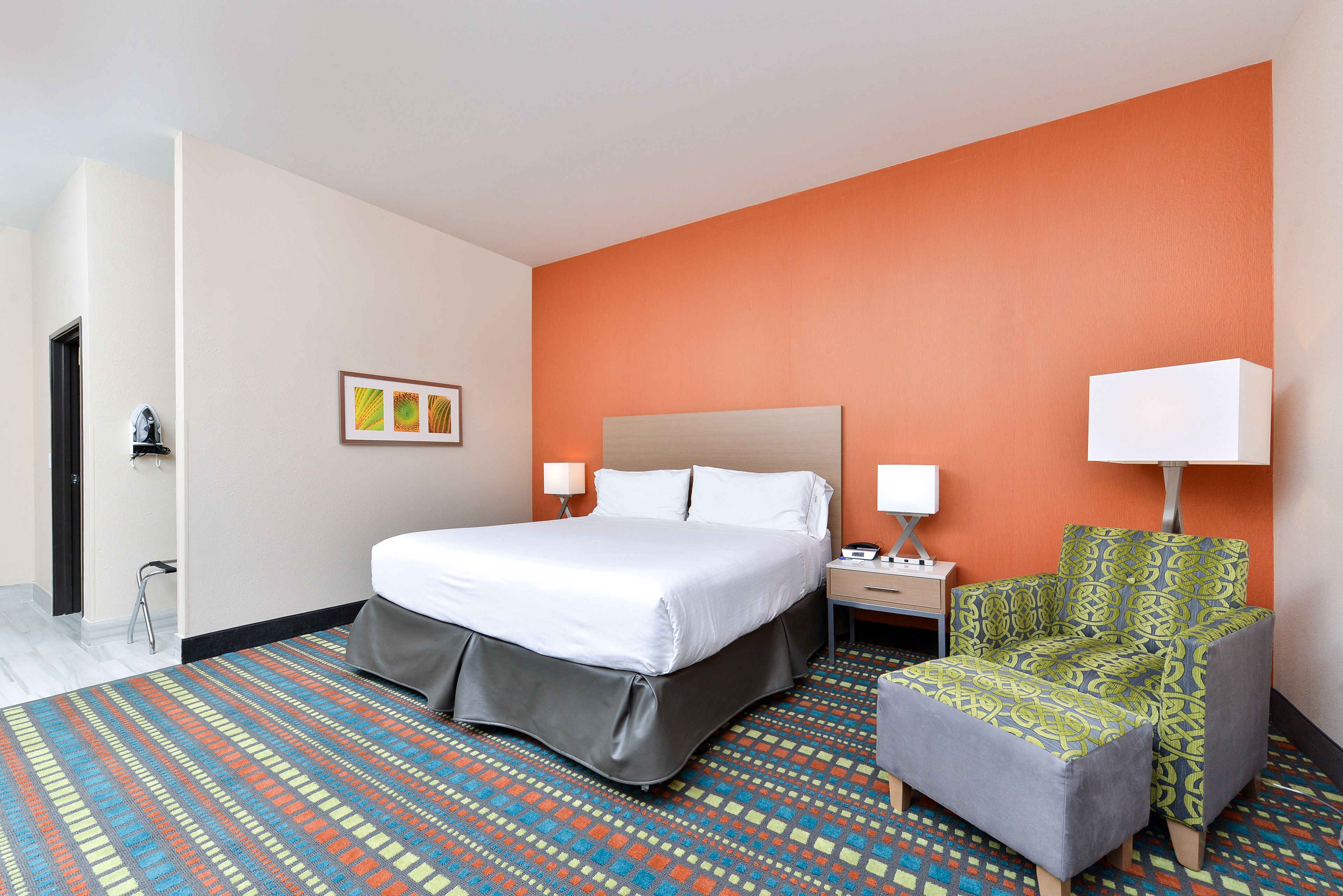 A hotel room with a bed, a chair, a nightstand, and a lamp.