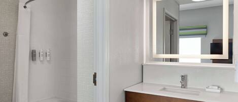 A modern bathroom with a glass-enclosed shower, a wooden vanity with a sink, and a mirror with a light above it.