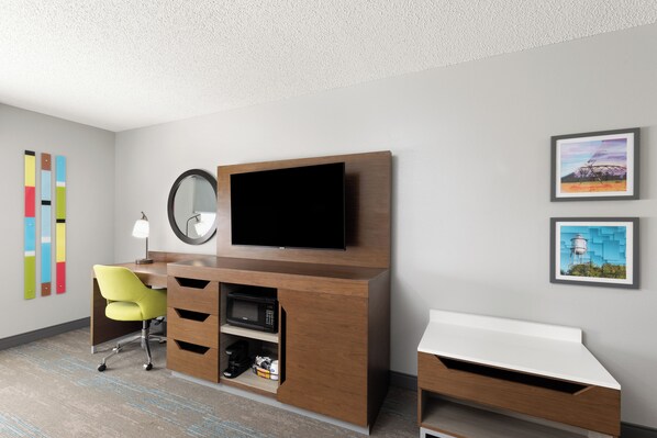 A modern hotel room with a wooden desk, a flat-screen TV, a yellow chair, a small coffee machine, and two framed pictures on the wall. - Hampton Inn & Suites Dothan (Dothan)