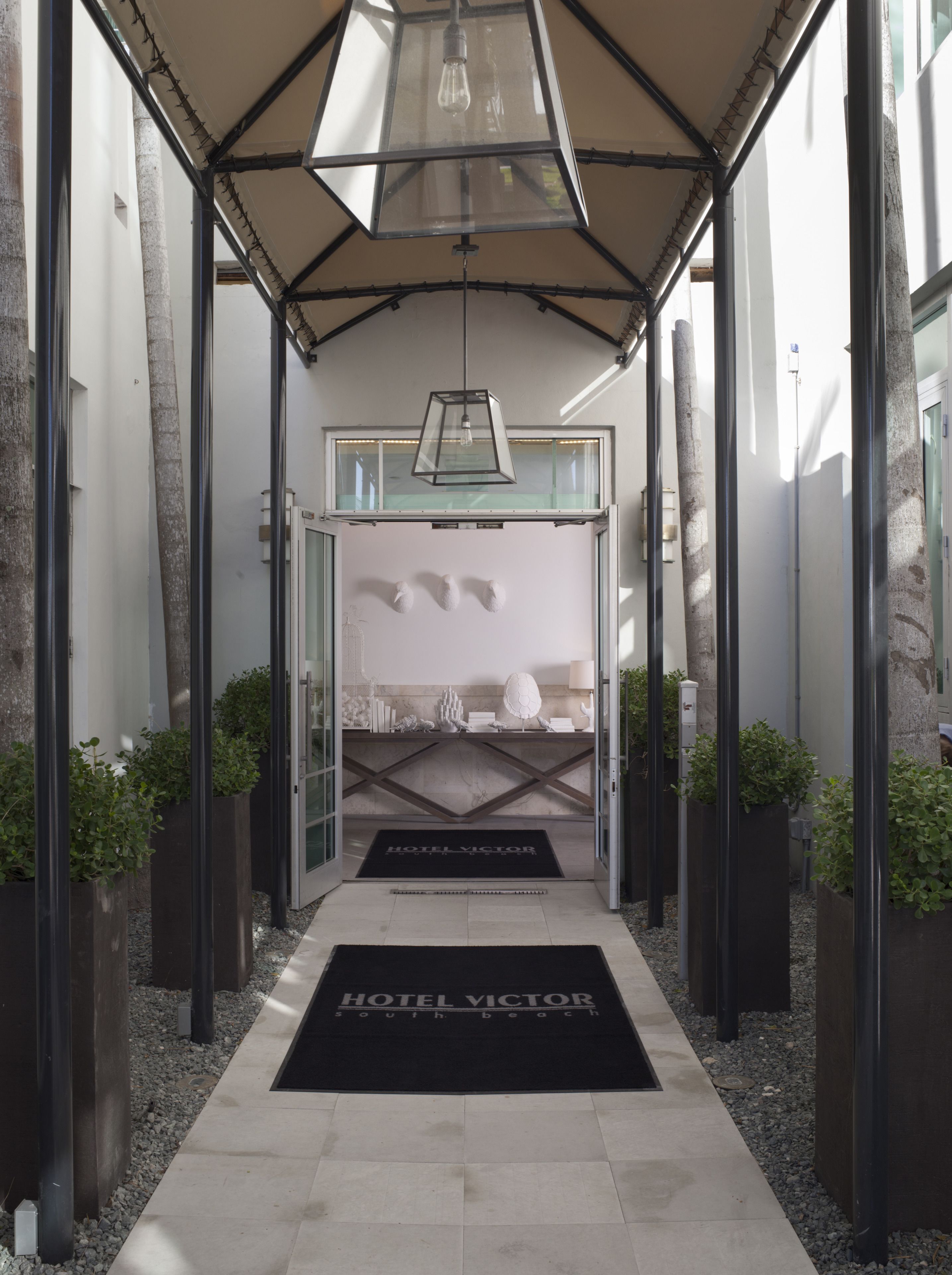 A hotel entrance with a modern design, featuring a glass door, a black doormat, and a geometric ceiling structure.
