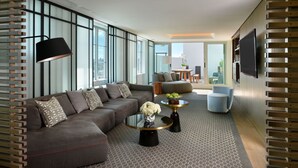 A modern living room with a sectional sofa, a round coffee table, and a flat-screen TV mounted on the wall. - Hotel Victor (Miami Beach)
