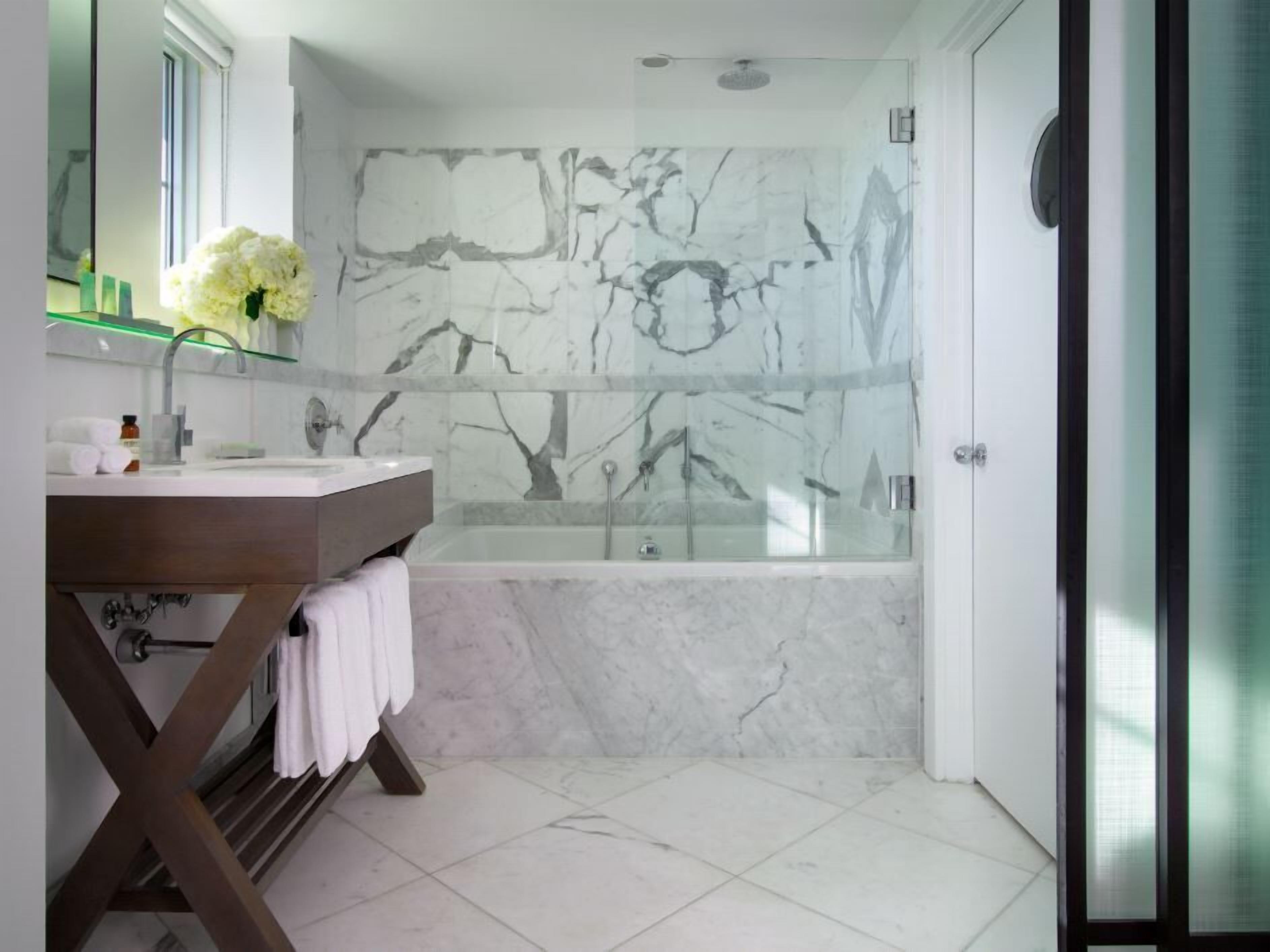 A modern bathroom with a marble wall, a glass-enclosed shower, and a wooden vanity.