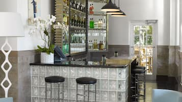 Uma área de bar com bancada de mármore, dois bancos e diversos frascos e copos.