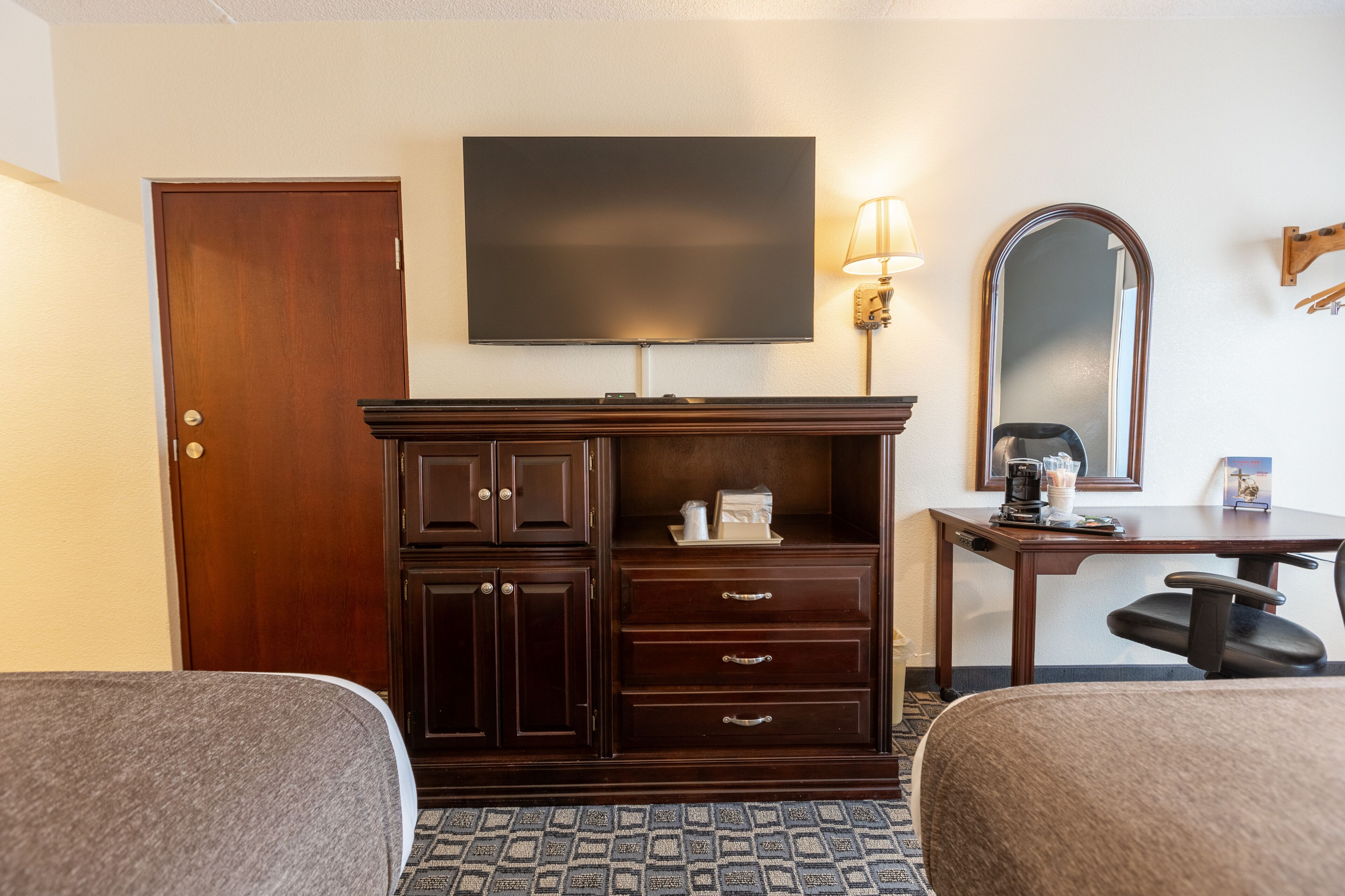 A hotel room with two beds, a TV, a desk with a lamp, a coffee maker, and a mirror.