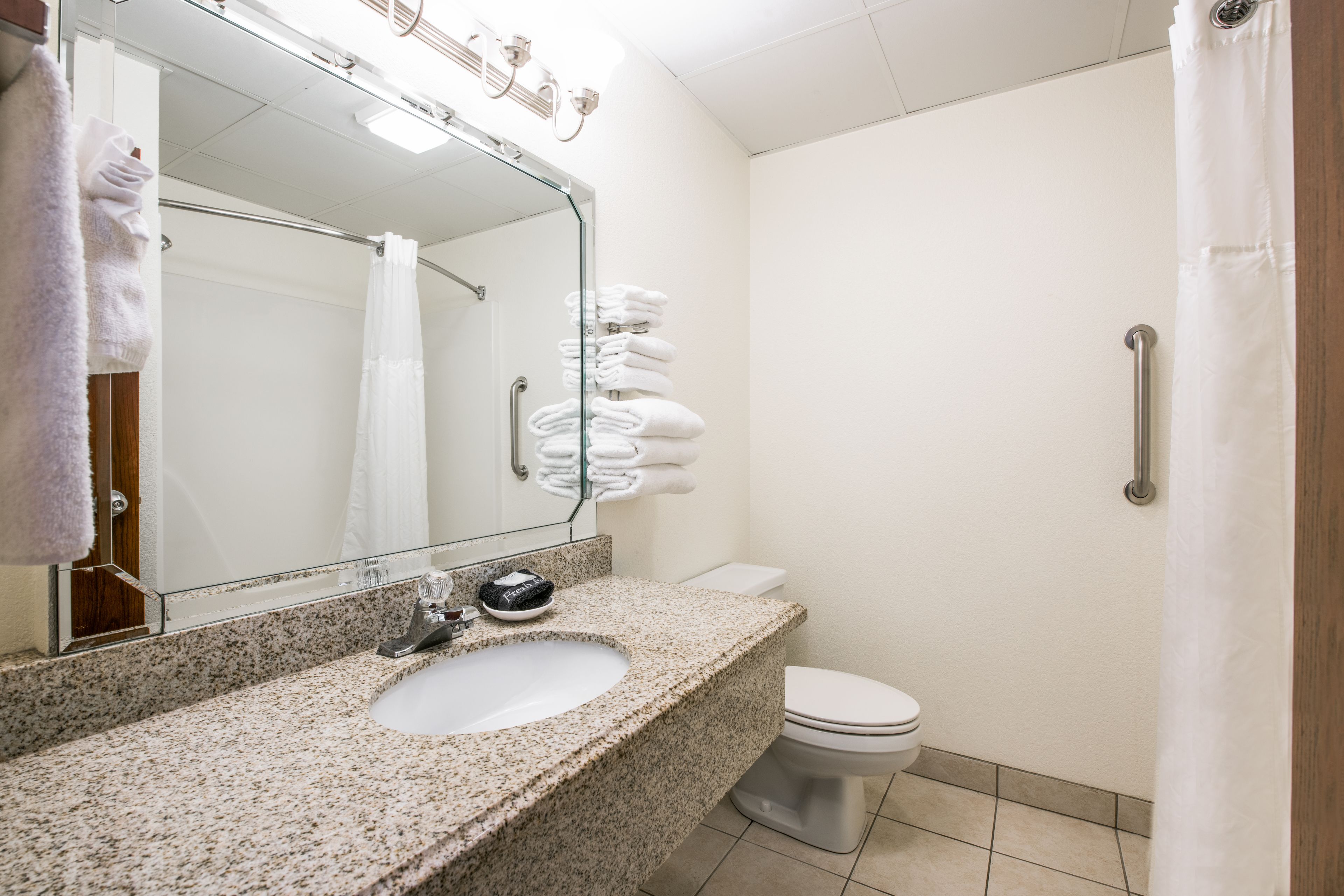 A bathroom with a granite countertop sink, a mirror, a toilet, and a shower curtain.