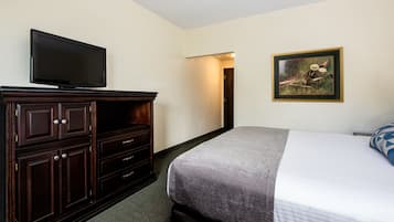 Ein Hotelzimmer mit einem Bett, einem Schminktisch, einem Fernseher und einem gerahmten Bild an der Wand.