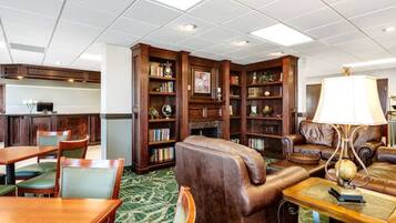 A library with leather sofas, wooden bookshelves, and a dining area with a green carpet.