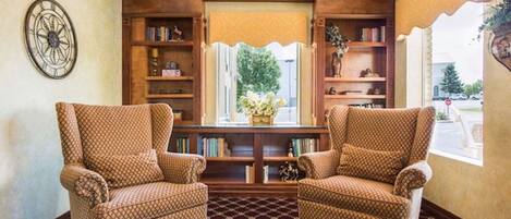 A room with two patterned armchairs, a wooden bookshelf, and a window with a view of greenery.