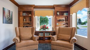 Una habitación con dos sillones con estampado, una estantería de madera y una ventana con vista a un estacionamiento.