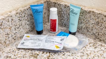 Un meuble-lavabo de salle de bain avec des produits de toilette, notamment deux tubes de shampooing « Alure Therapy », un flacon de lotion « Hydra-Lant » et un paquet de lingettes démaquillantes douces.