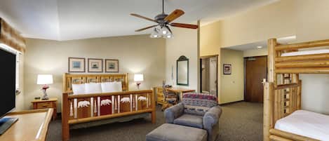 A hotel room with a wooden bed, a sofa, a desk, a chair, a ceiling fan, and a bunk bed.