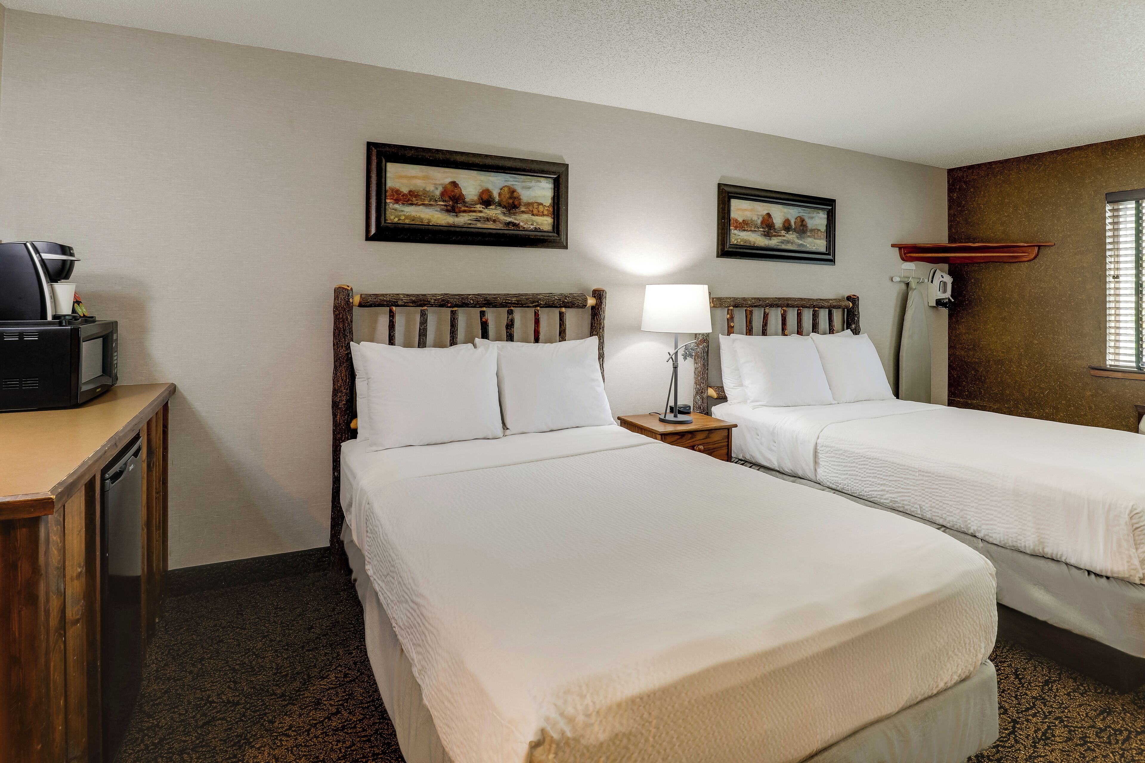 A hotel room with two beds, a desk with a coffee maker, and two framed pictures on the wall.